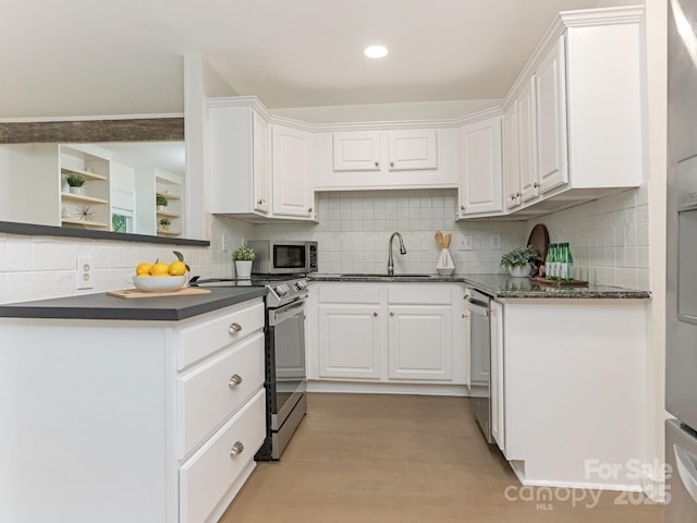 kitchen with stainless steel appliances, a sink, dark countertops, white cabinetry, and recessed lighting