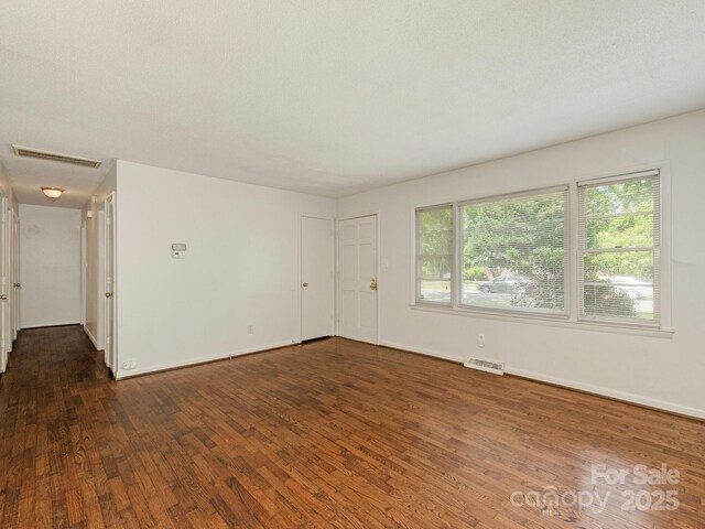 unfurnished room with visible vents, a healthy amount of sunlight, and dark wood-style floors