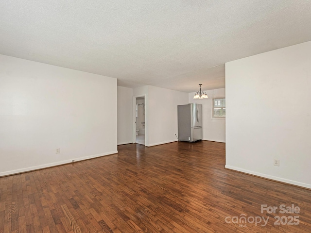 spare room with a chandelier, a textured ceiling, baseboards, and dark wood-style floors