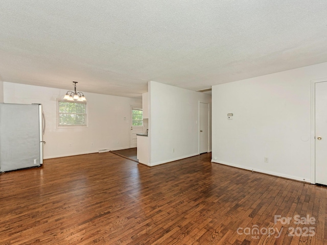 unfurnished living room with dark wood finished floors, an inviting chandelier, and a textured ceiling