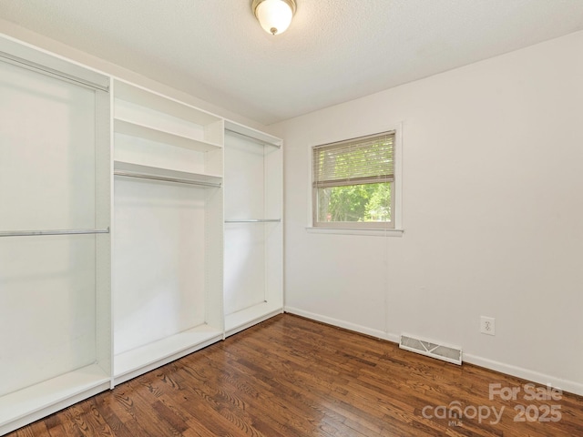 unfurnished bedroom with a closet, visible vents, wood finished floors, and baseboards