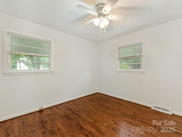 empty room featuring a wealth of natural light, baseboards, visible vents, and wood finished floors