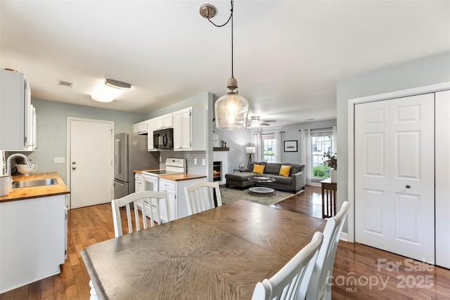 dining area featuring a ceiling fan, wood finished floors, and a lit fireplace