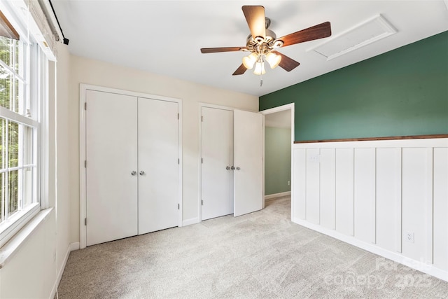 unfurnished bedroom featuring light carpet, two closets, a ceiling fan, and baseboards