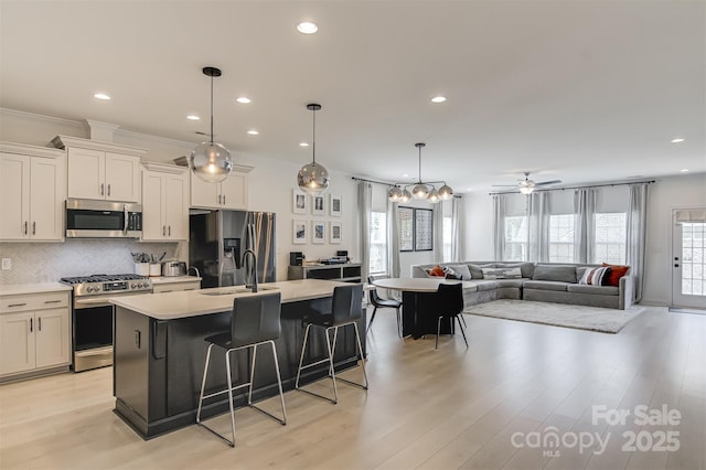 kitchen with light countertops, stainless steel appliances, a kitchen bar, backsplash, and a center island with sink
