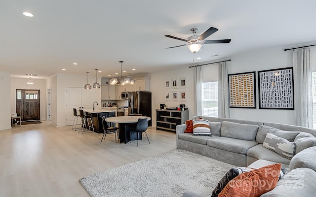 living room with light wood finished floors, ceiling fan with notable chandelier, recessed lighting, and visible vents