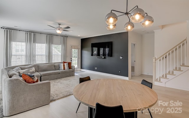 living room featuring stairway, baseboards, ceiling fan with notable chandelier, and light wood-type flooring