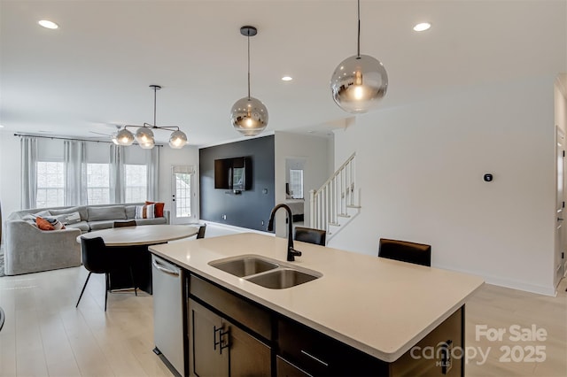 kitchen with stainless steel dishwasher, a sink, open floor plan, and light countertops