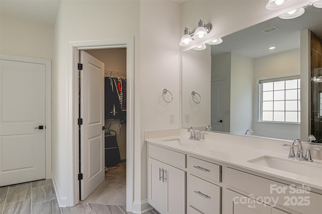 full bath featuring double vanity, a walk in closet, visible vents, and a sink