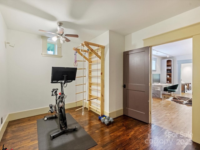 exercise area featuring dark wood finished floors, a ceiling fan, and baseboards