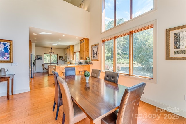 dining space featuring a chandelier, light wood-style flooring, baseboards, and a towering ceiling