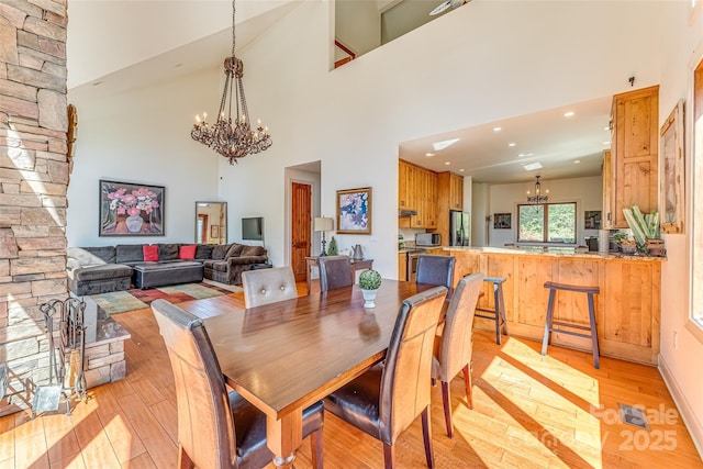 dining space featuring a chandelier, light wood-style flooring, a high ceiling, and recessed lighting