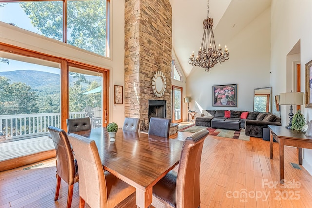 dining area with light wood-style flooring, an inviting chandelier, visible vents, high vaulted ceiling, and a fireplace