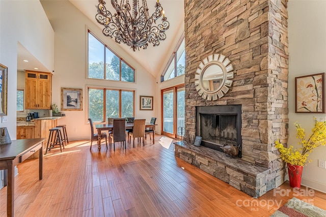 dining area with wood finished floors, high vaulted ceiling, a fireplace, a notable chandelier, and baseboards