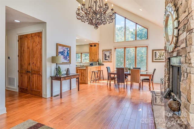 dining area with a notable chandelier, light wood-style flooring, visible vents, a towering ceiling, and a fireplace