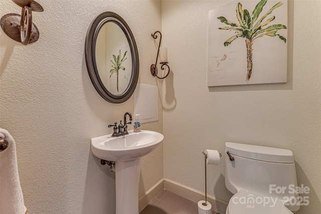 half bath with toilet, tile patterned flooring, and baseboards