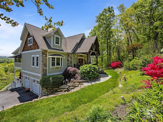 view of property exterior with roof with shingles, a garage, aphalt driveway, a yard, and stone siding