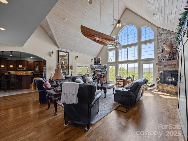 living room with a ceiling fan, high vaulted ceiling, wood finished floors, and a fireplace