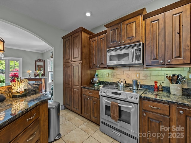 kitchen with dark stone counters, stainless steel appliances, arched walkways, and tasteful backsplash