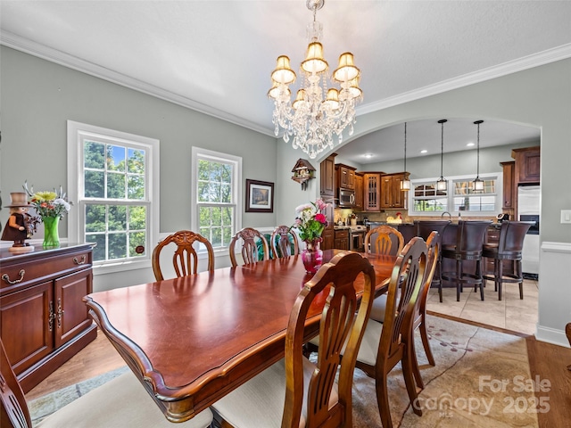 dining space featuring crown molding, baseboards, a chandelier, arched walkways, and light wood-style flooring