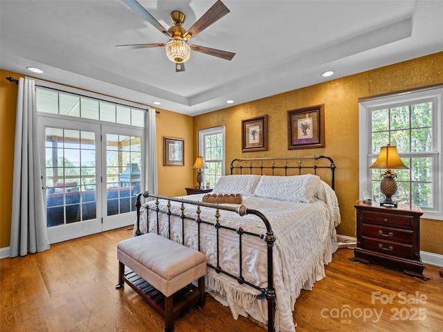bedroom with access to outside, wood finished floors, and a raised ceiling