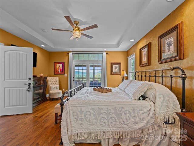 bedroom with multiple windows, a tray ceiling, and wood finished floors