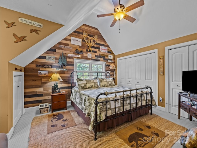 bedroom with carpet floors, wood walls, two closets, baseboards, and lofted ceiling