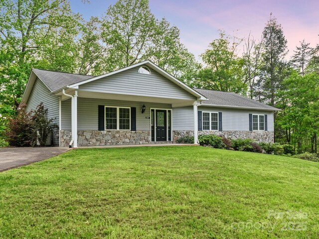 single story home with a shingled roof, a porch, a front lawn, and stone siding