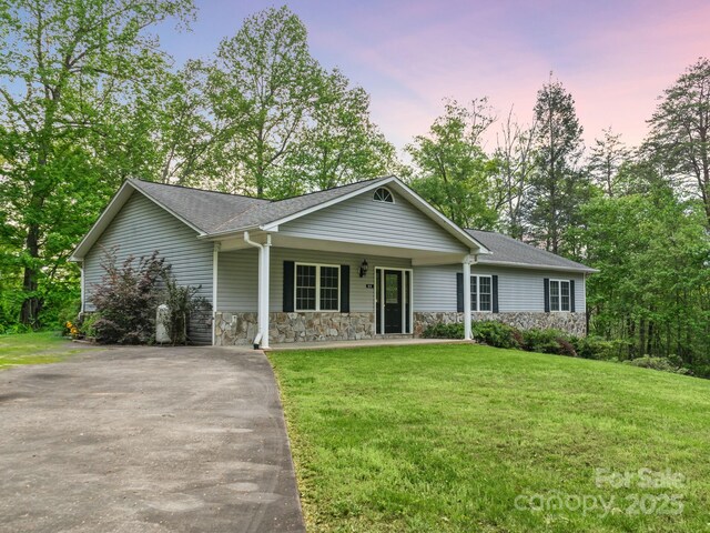 ranch-style house with covered porch, roof with shingles, a front yard, aphalt driveway, and stone siding