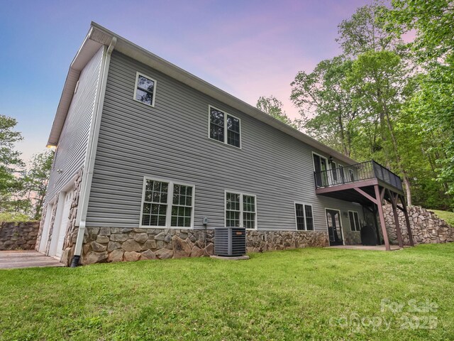 back of house at dusk featuring a lawn, a garage, central AC, and stone siding