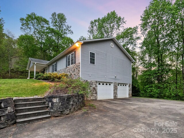 view of home's exterior featuring a yard, an attached garage, stone siding, and aphalt driveway
