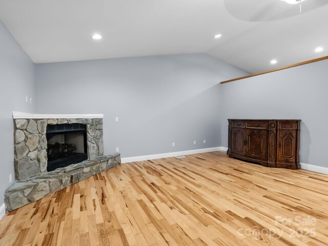 unfurnished living room with wood finished floors, baseboards, a stone fireplace, recessed lighting, and vaulted ceiling