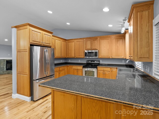 kitchen featuring dark countertops, a sink, a peninsula, lofted ceiling, and stainless steel appliances