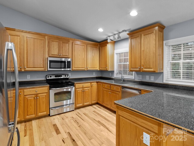 kitchen featuring a sink, light wood-style flooring, appliances with stainless steel finishes, and dark countertops