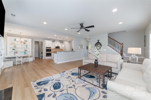 living area featuring light wood-style floors, ceiling fan with notable chandelier, recessed lighting, visible vents, and stairway