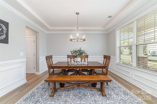 dining area featuring wainscoting, a raised ceiling, light wood-style floors, a chandelier, and visible vents