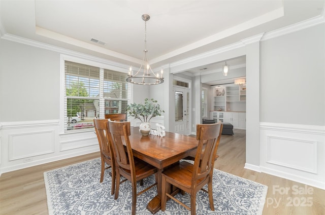 dining area with visible vents, a notable chandelier, a tray ceiling, and light wood-type flooring