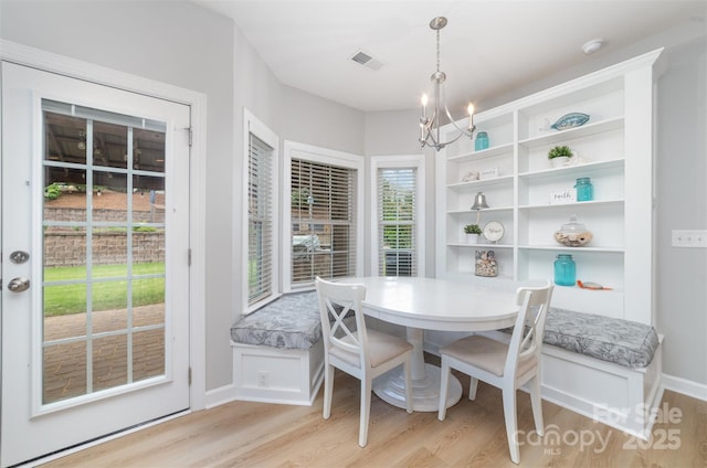 dining room featuring light wood-style floors, baseboards, visible vents, and a notable chandelier