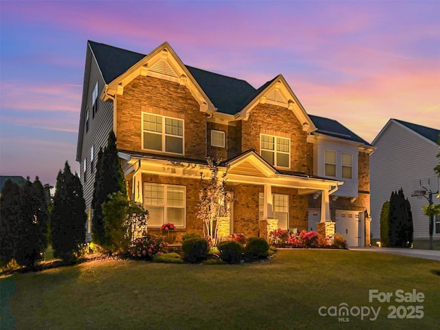 craftsman-style house with covered porch, driveway, a garage, a yard, and stone siding