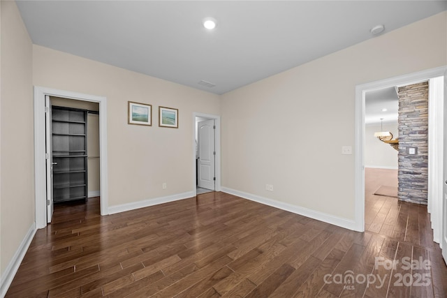 unfurnished bedroom with a walk in closet, baseboards, and dark wood-style flooring
