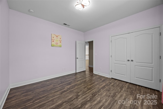 unfurnished bedroom with baseboards, a closet, dark wood-style floors, and visible vents