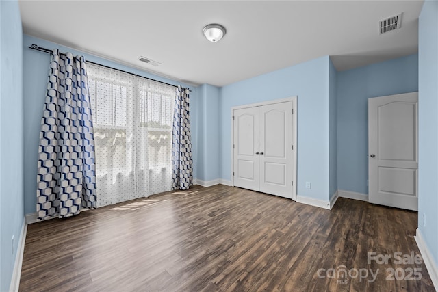 unfurnished bedroom featuring baseboards, a closet, wood finished floors, and visible vents
