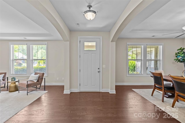 entryway with arched walkways, dark wood finished floors, and a tray ceiling
