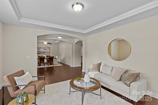 living area with crown molding, arched walkways, baseboards, and wood finished floors