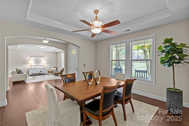 dining area featuring visible vents, a ceiling fan, baseboards, a tray ceiling, and arched walkways