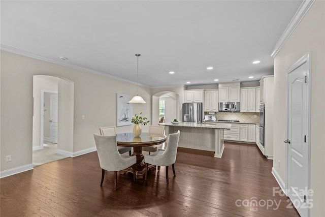 dining area featuring crown molding, arched walkways, baseboards, and dark wood-style floors
