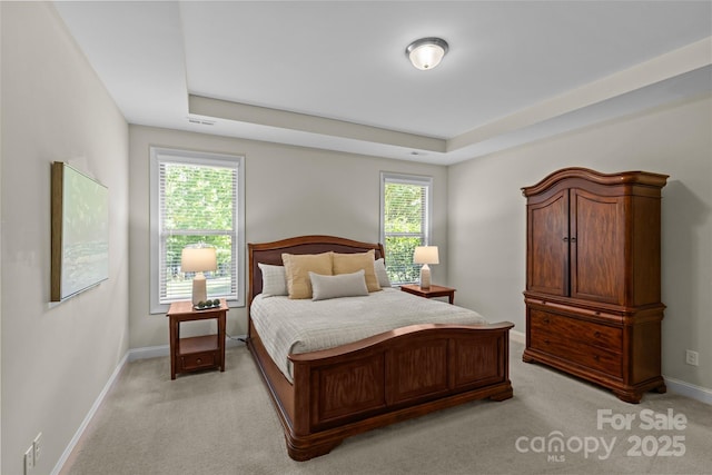 bedroom featuring visible vents, baseboards, a tray ceiling, and light carpet
