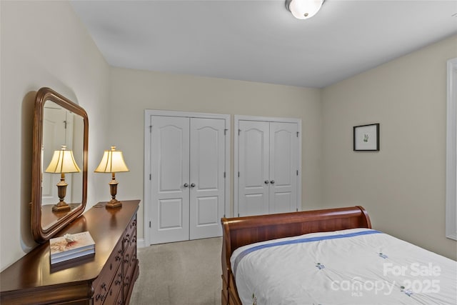 bedroom featuring baseboards, light carpet, and two closets