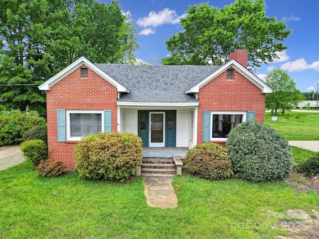 view of front facade with a porch, a chimney, a front yard, brick siding, and a shingled roof