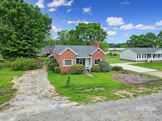 bungalow-style home with brick siding, a chimney, a front yard, and aphalt driveway
